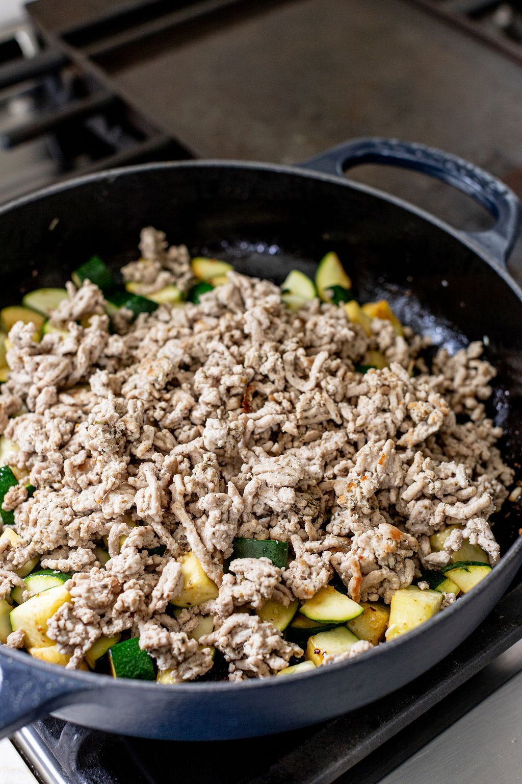 Cooked ground turkey and diced zucchini in a skillet on a stove.