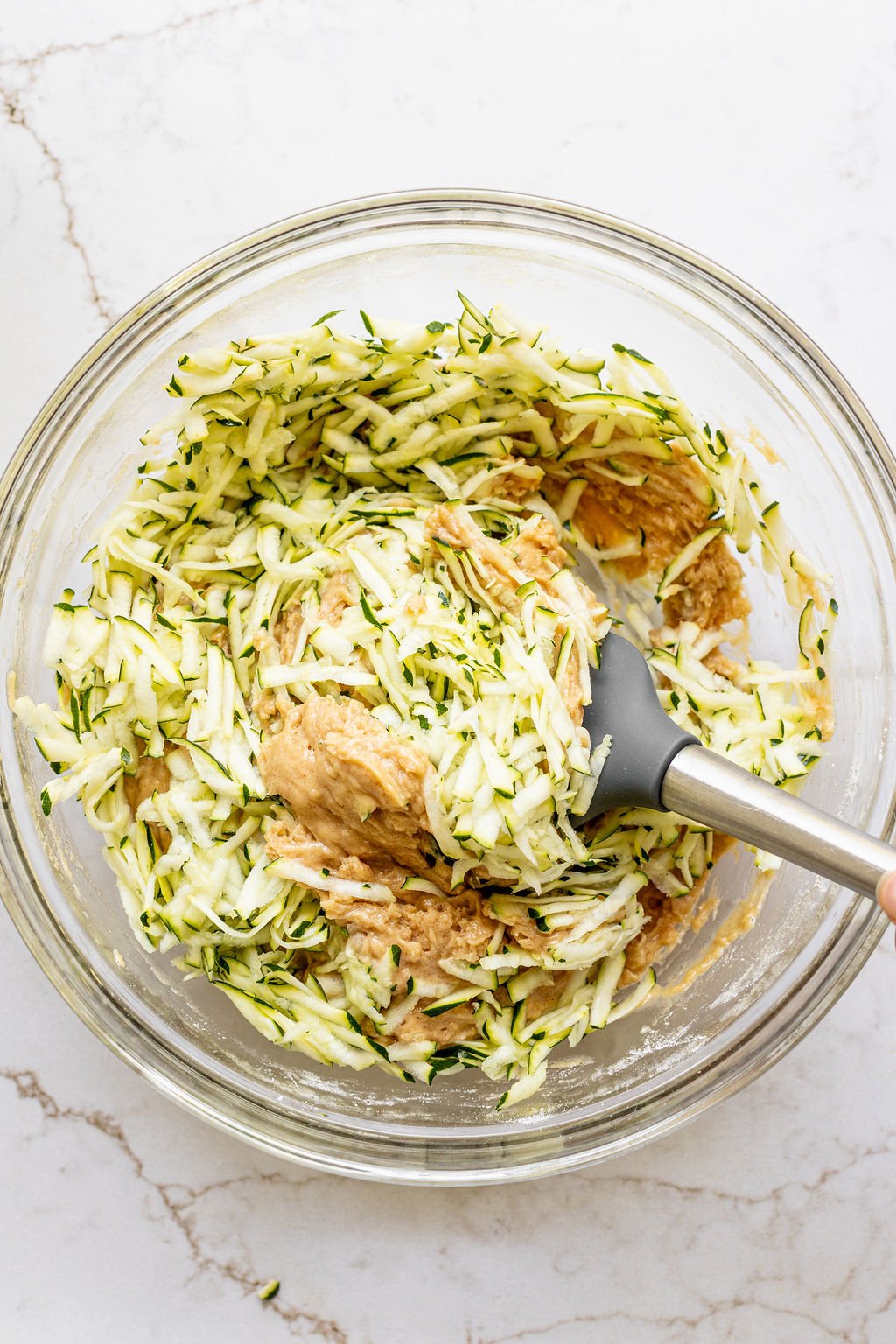 Shredded zucchini in a mixing bowl with bread batter.