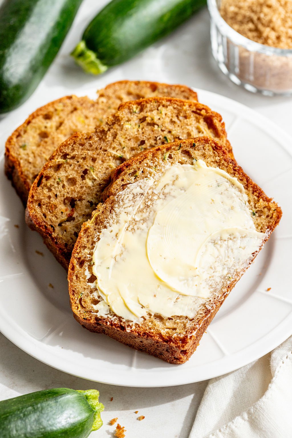 A slice of zucchini bread covered in butter on a plate.