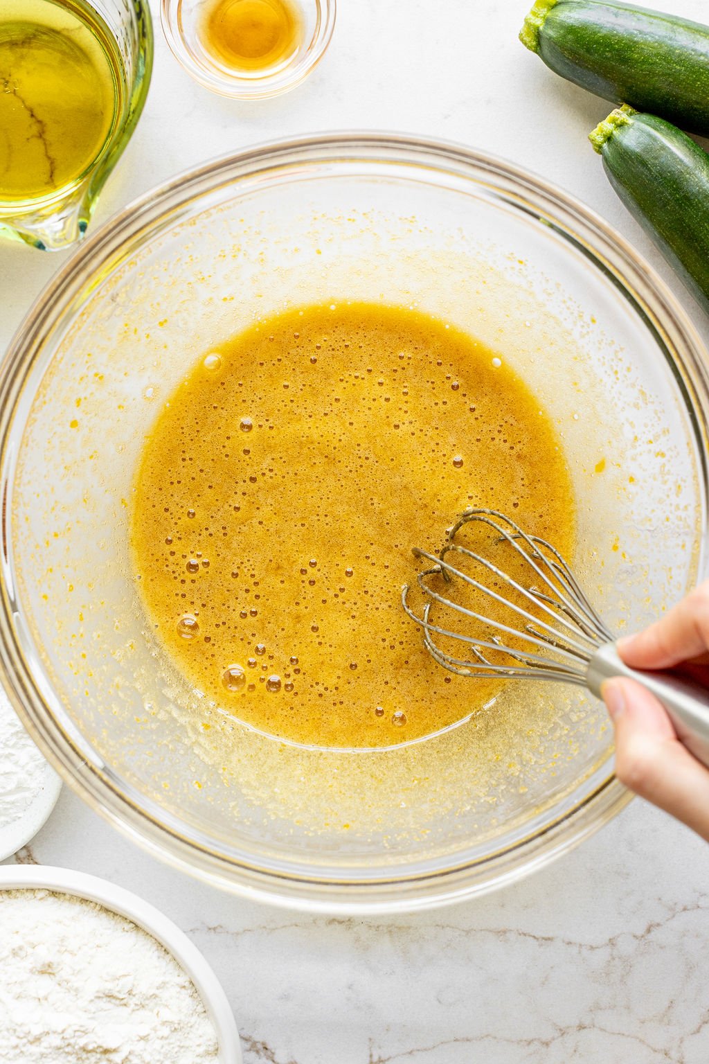 A hand whisking a light brown, wet mixture in a bowl.