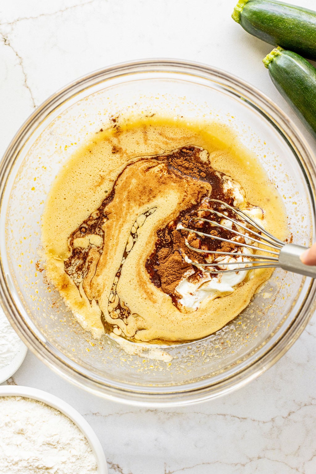 A hand whisking cinnamon and yogurt into eggs and oil.