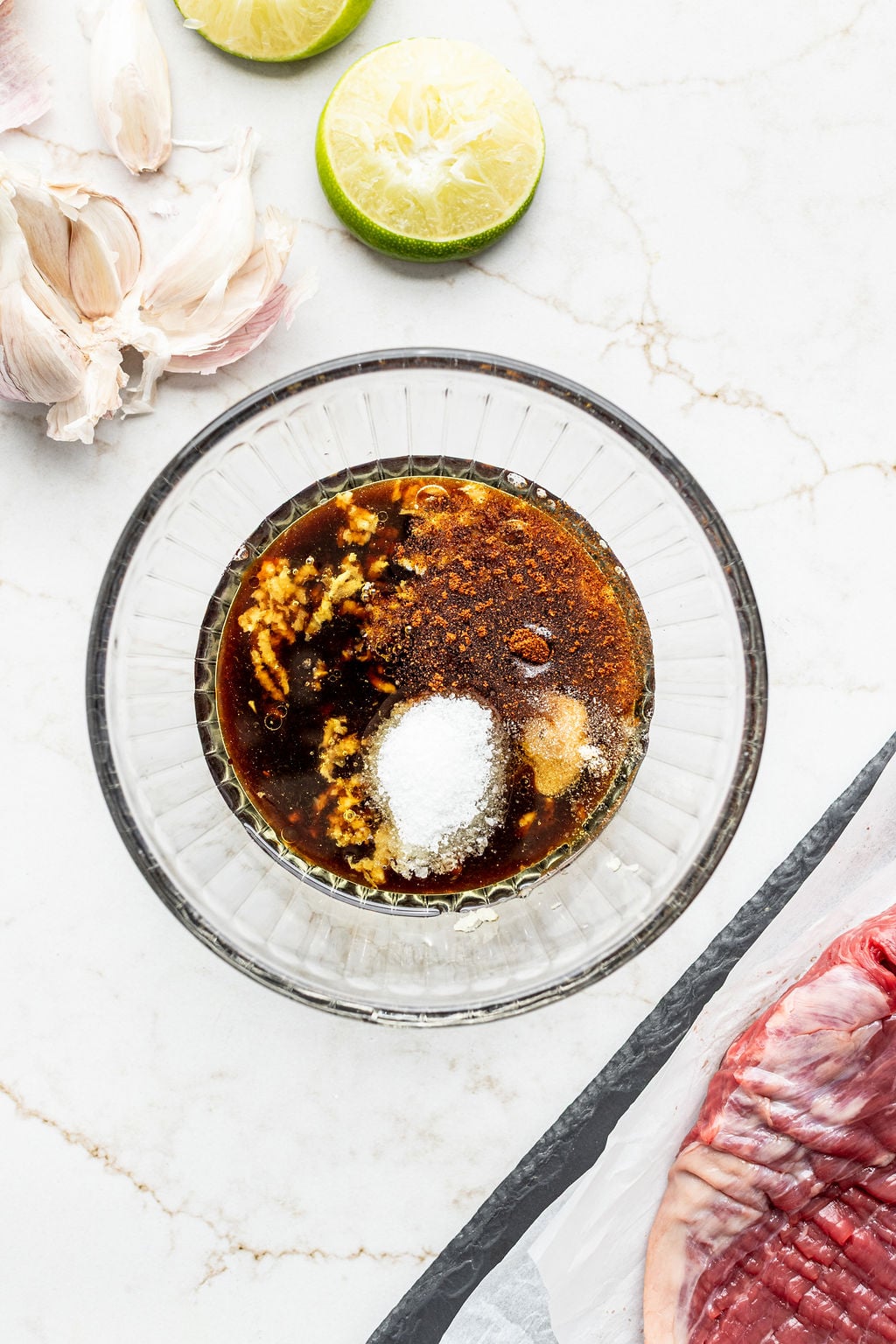 A bowl filled with soy sauce, Worcestershire sauce, garlic, brown sugar, oil, lime juice, salt, and spices.