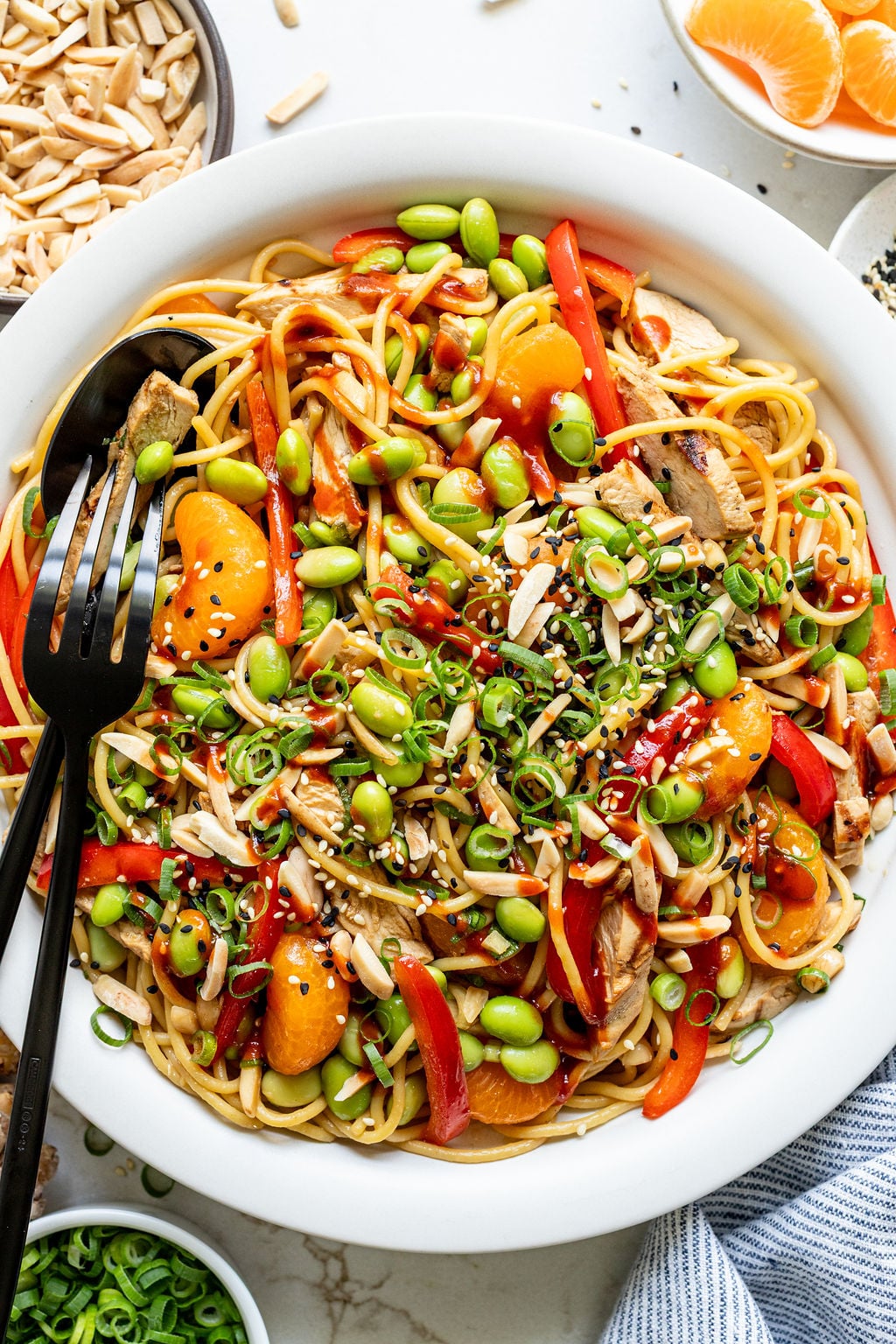Sesame seeds sprinkled on a dish of noodles, chicken, mandarins, chopped almonds, red bell peppers, and green onions.