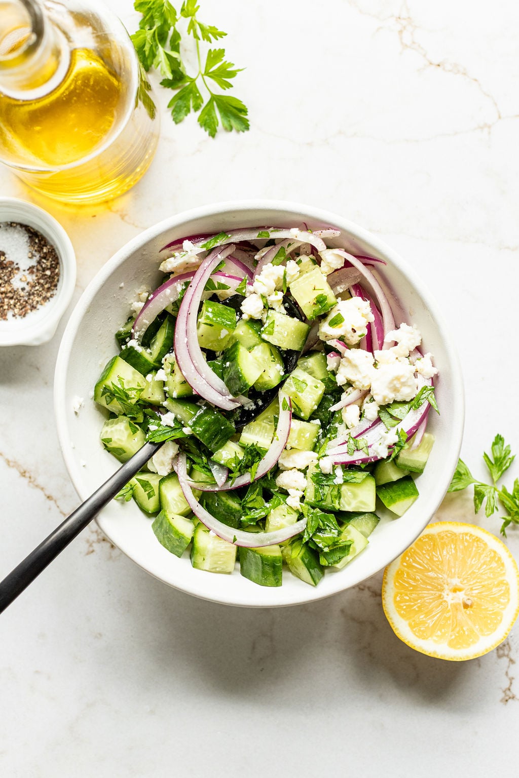 A bowl of cucumber salad with sliced red onions, feta cheese, and parsley.