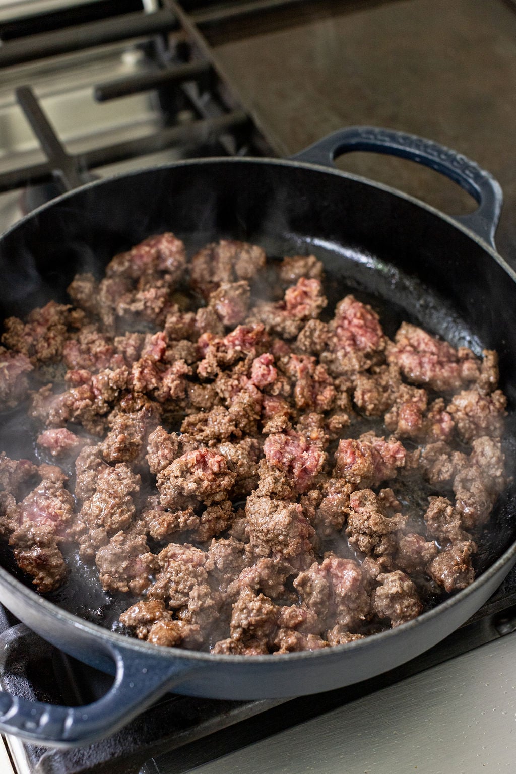 Ground beef browning in a black cast iron skillet on a stove.