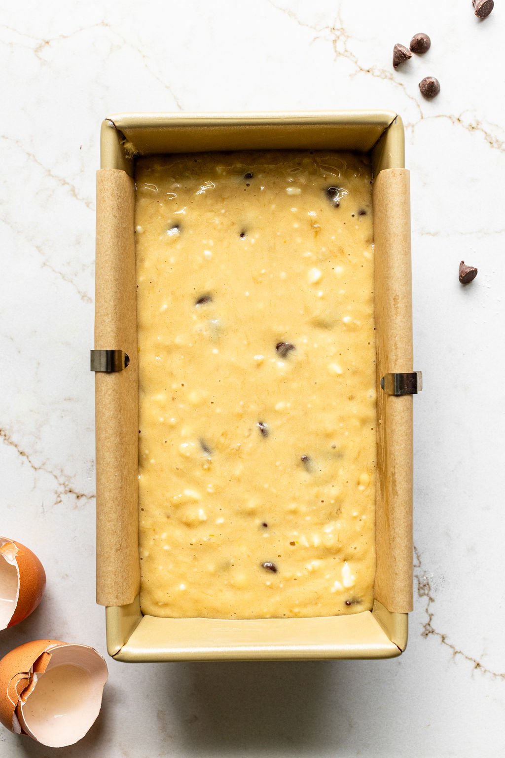 A loaf pan filled with banana bread batter with chocolate chips, lined with parchment paper.