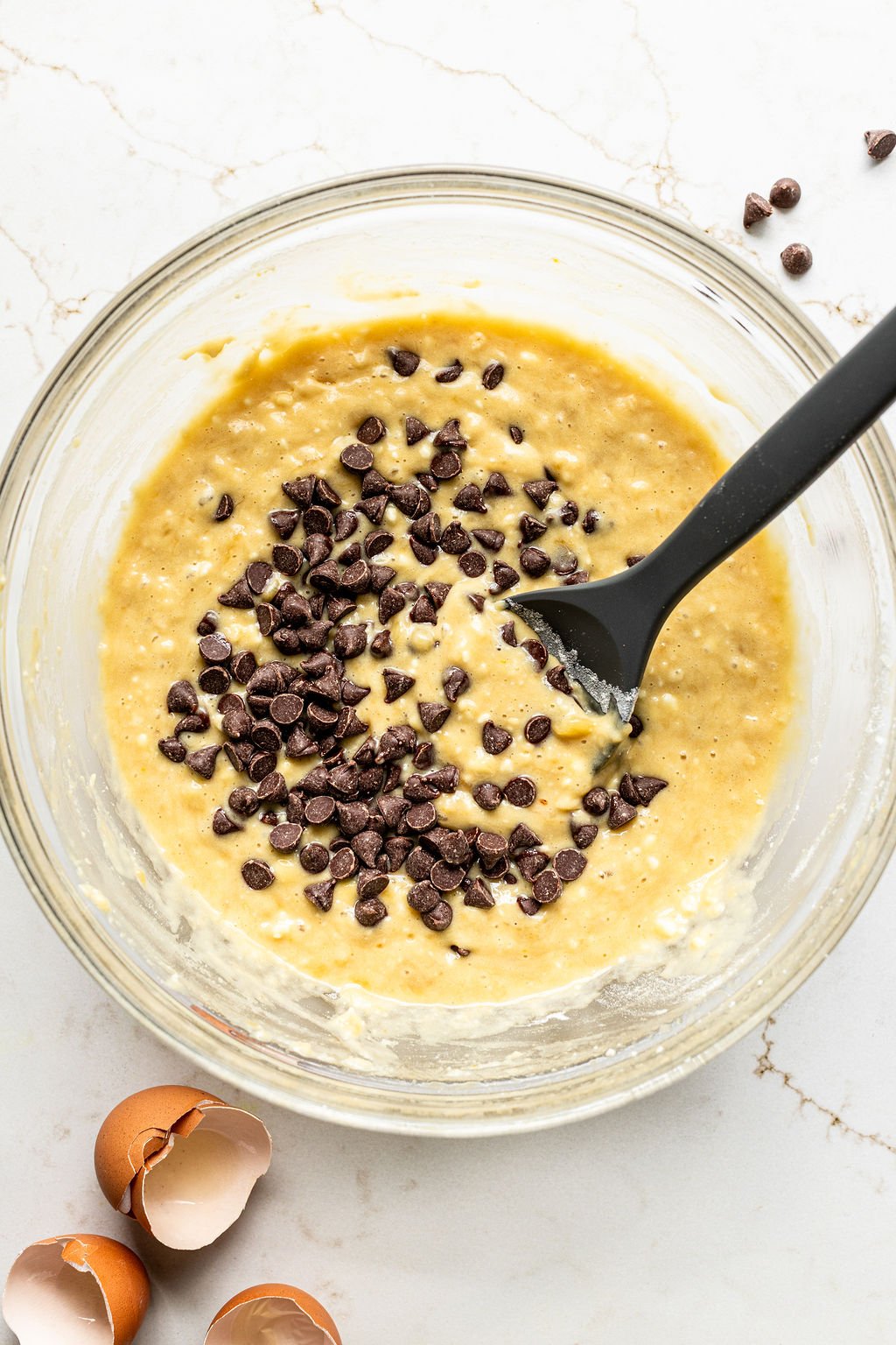 A glass bowl containing banana bread batter with chocolate chips being stirred in.