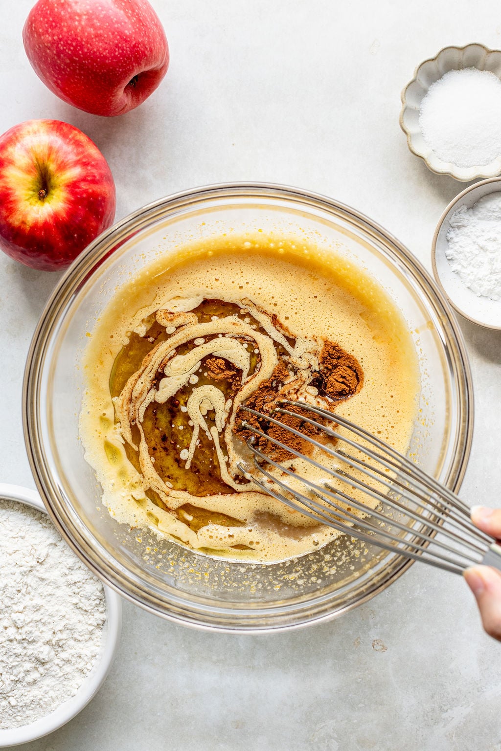 A hand whisks wet ingredients with cinnamon in a glass bowl.