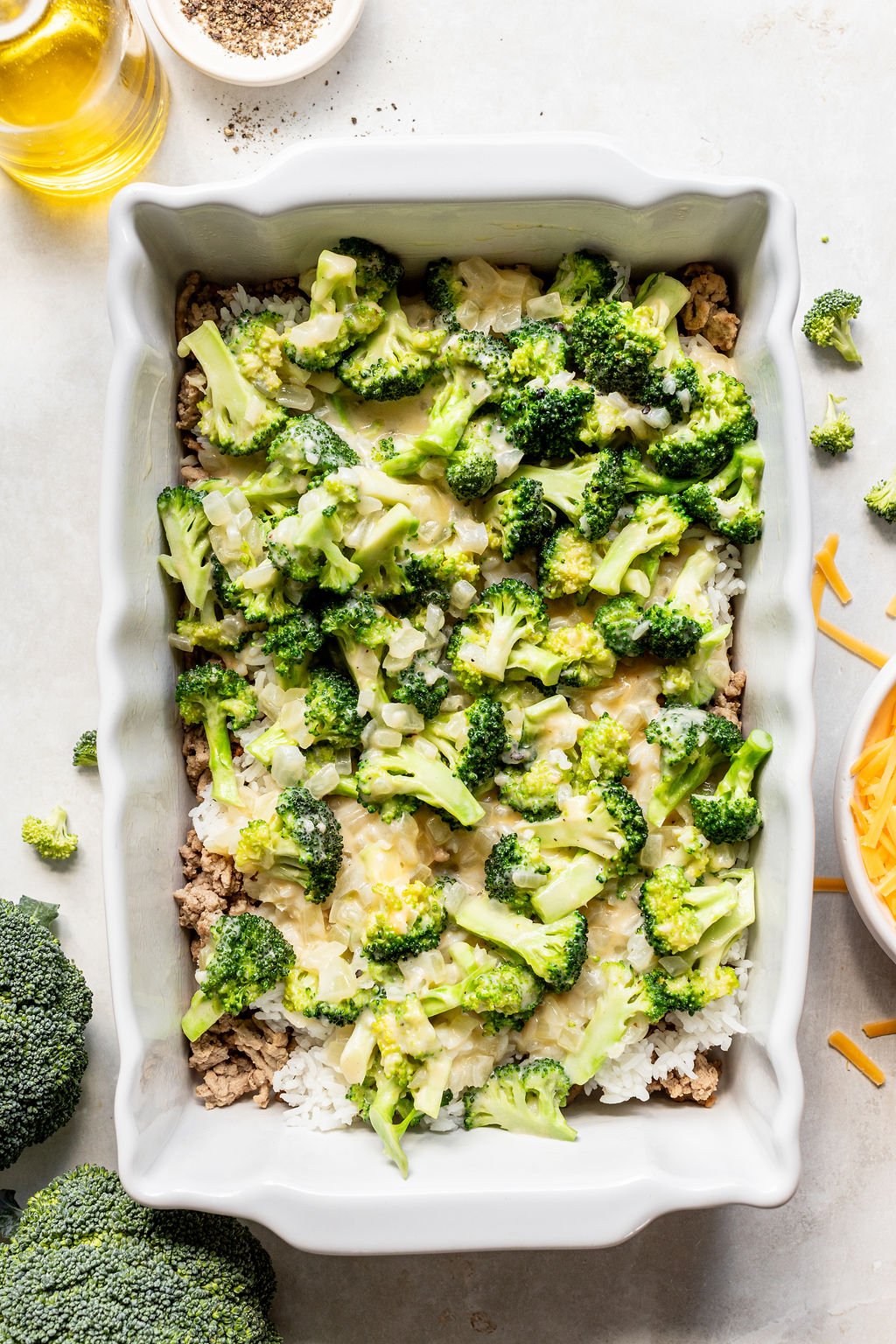 Rectangular baking dish filled with layers of white rice, ground meat, broccoli florets, and melted cheese.