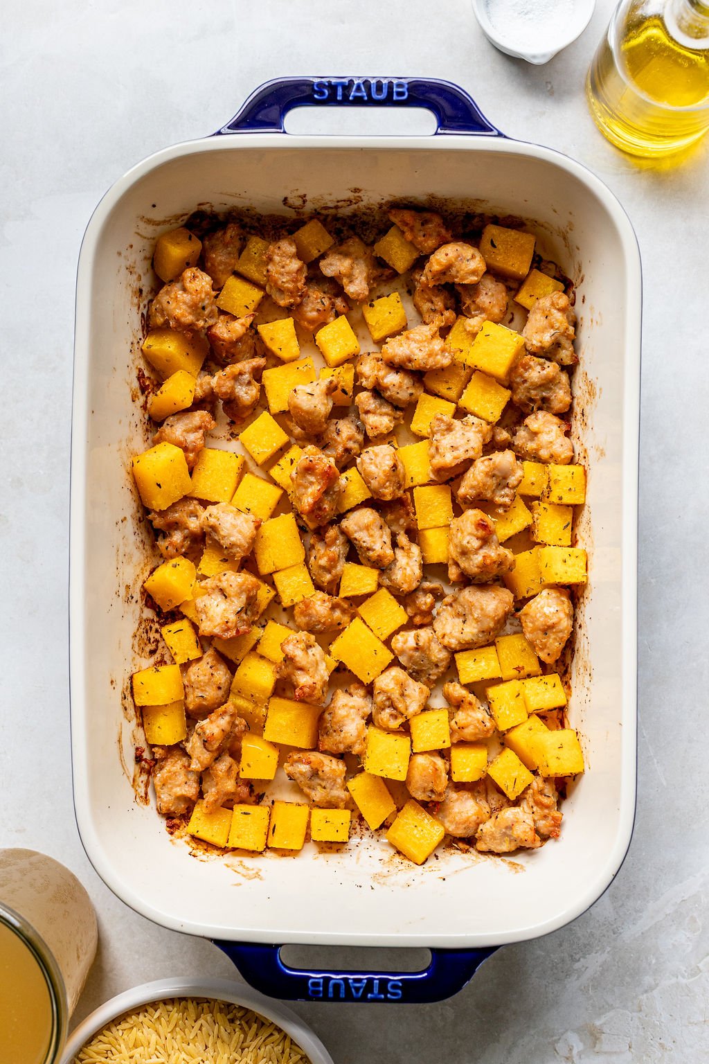 A baking dish filled with cooked chicken pieces and cubed butternut squash.