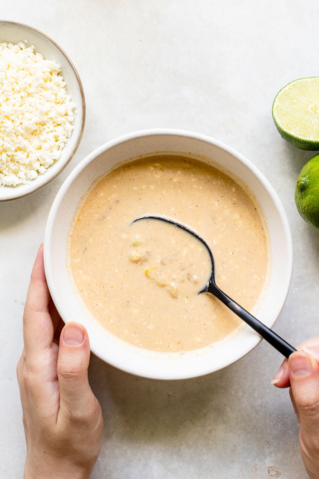 A hand holds a bowl of creamy soup or sauce being stirred with a black spoon.