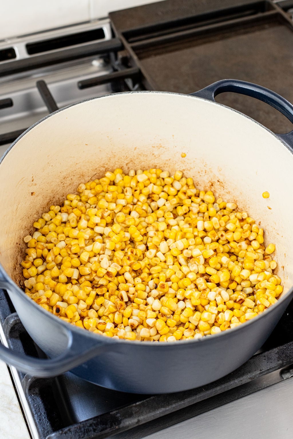 Corn kernels being saut&eacute;ed in a large blue Dutch oven on a stovetop.