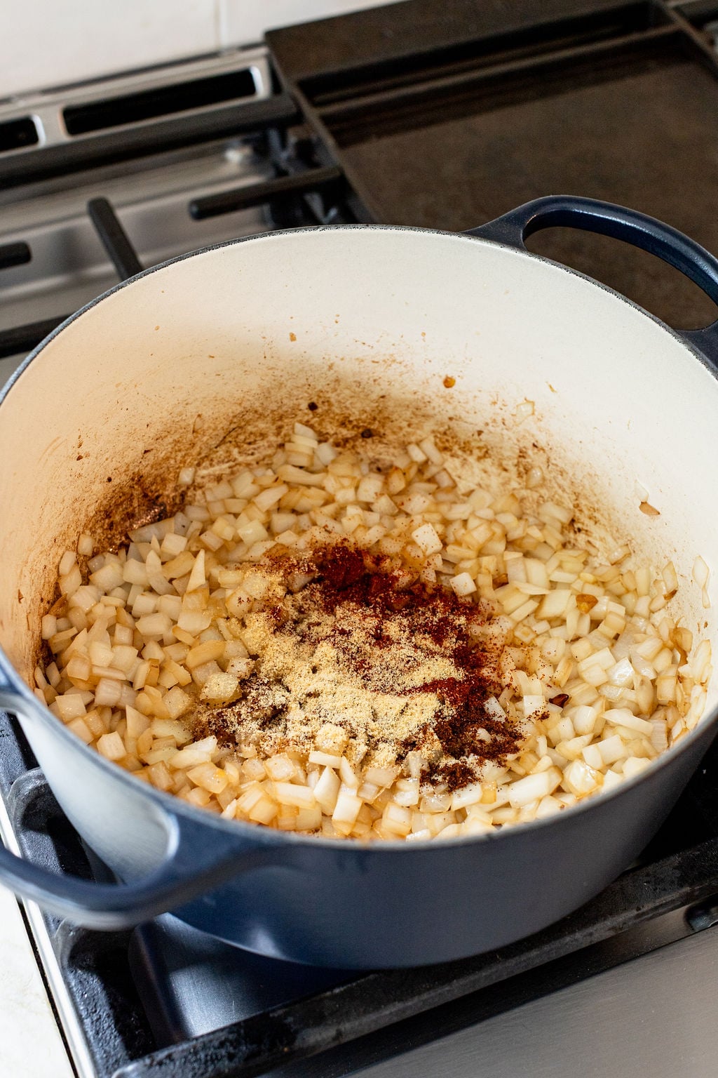Diced onions are saut&eacute;ing in a large pot on a stove, with ground spices sprinkled on top.