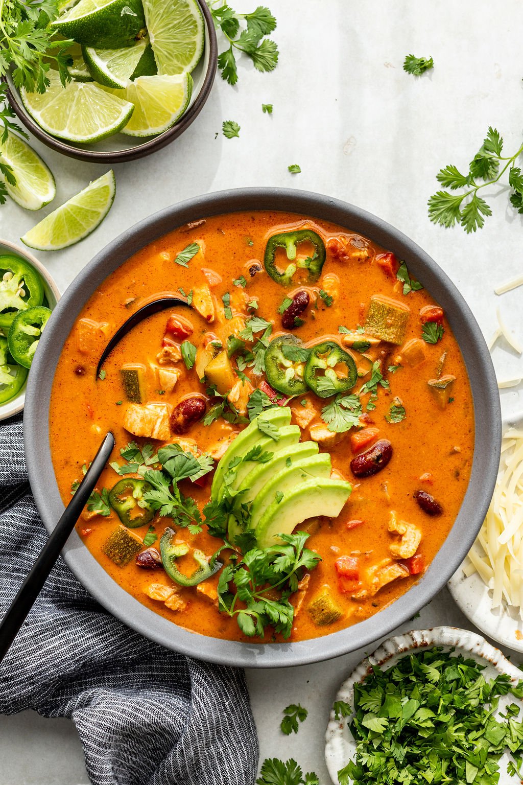 A bowl of creamy soup topped with sliced avocado, jalape&ntilde;os, cilantro, and black beans.