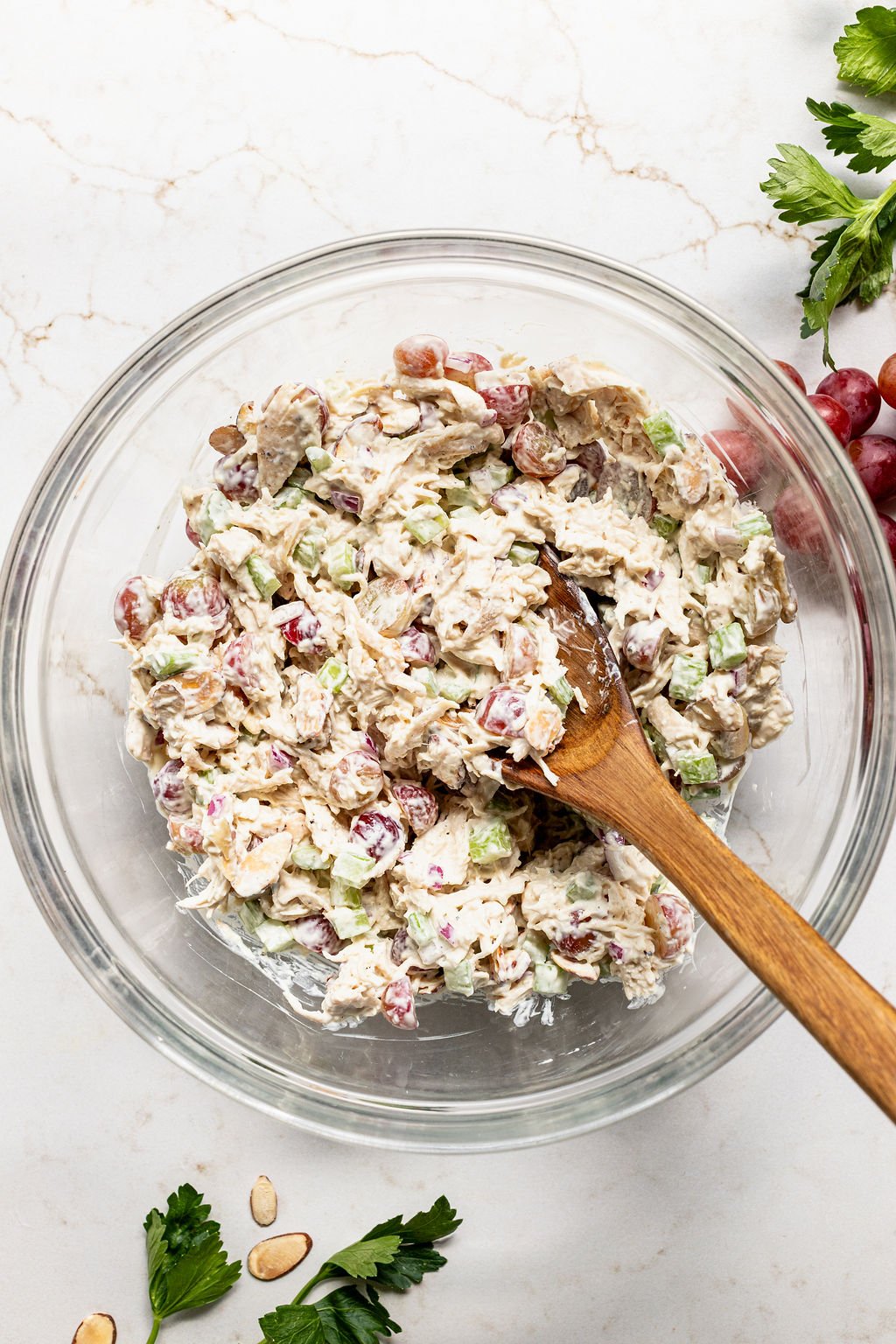 A glass bowl of chicken salad with grapes, celery, and sliced almonds, mixed with a creamy dressing.