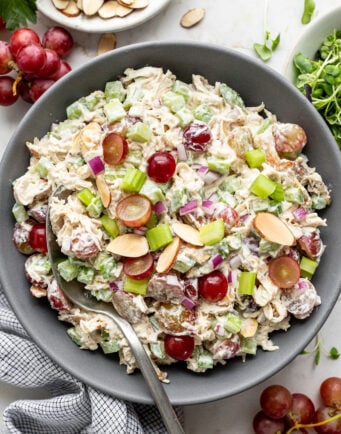 A bowl of chicken salad with grapes, celery, red onions, and sliced almonds, with a serving spoon.