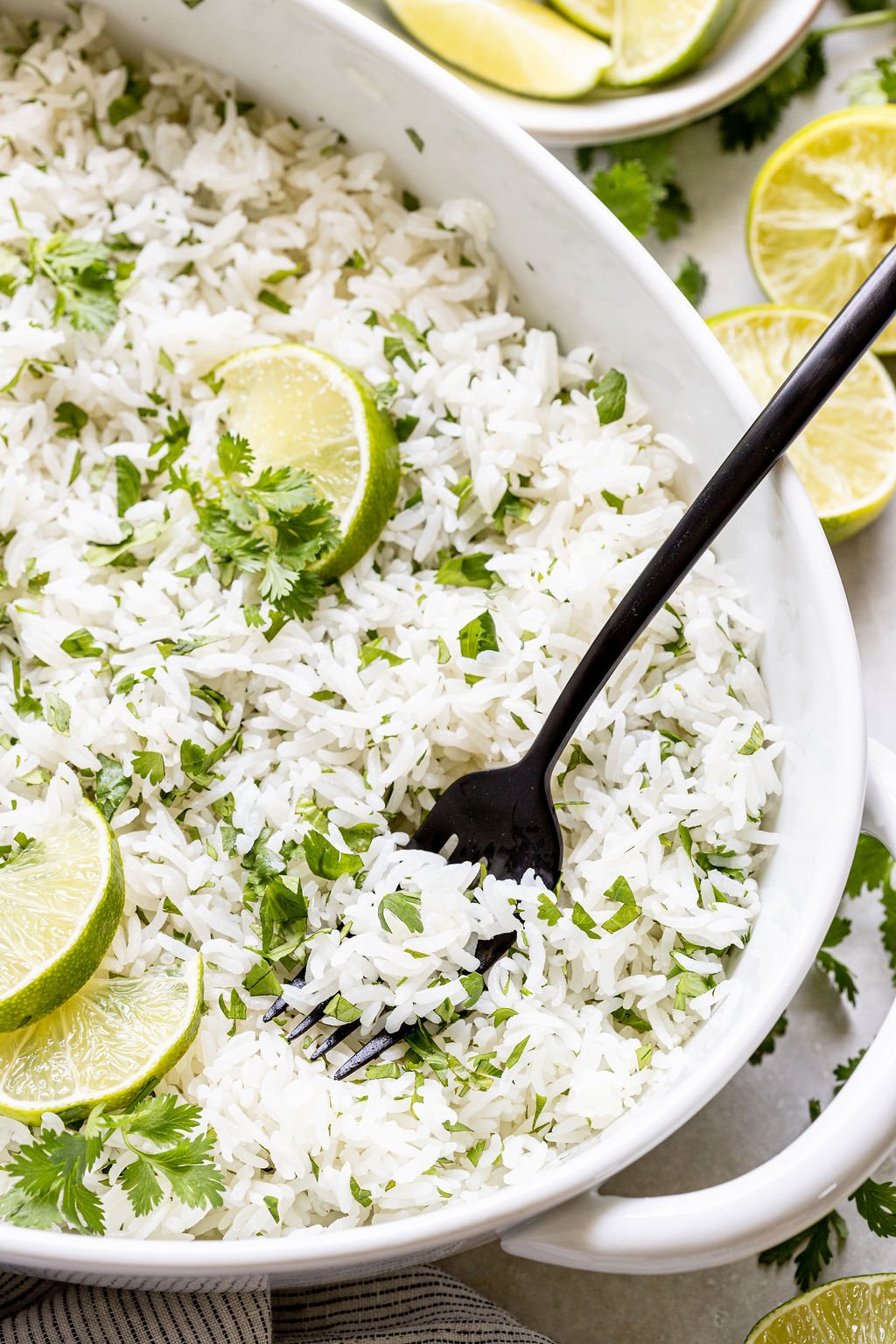 A black fork rests in a white dish filled with cilantro lime rice, garnished with lime wedges and fresh cilantro.