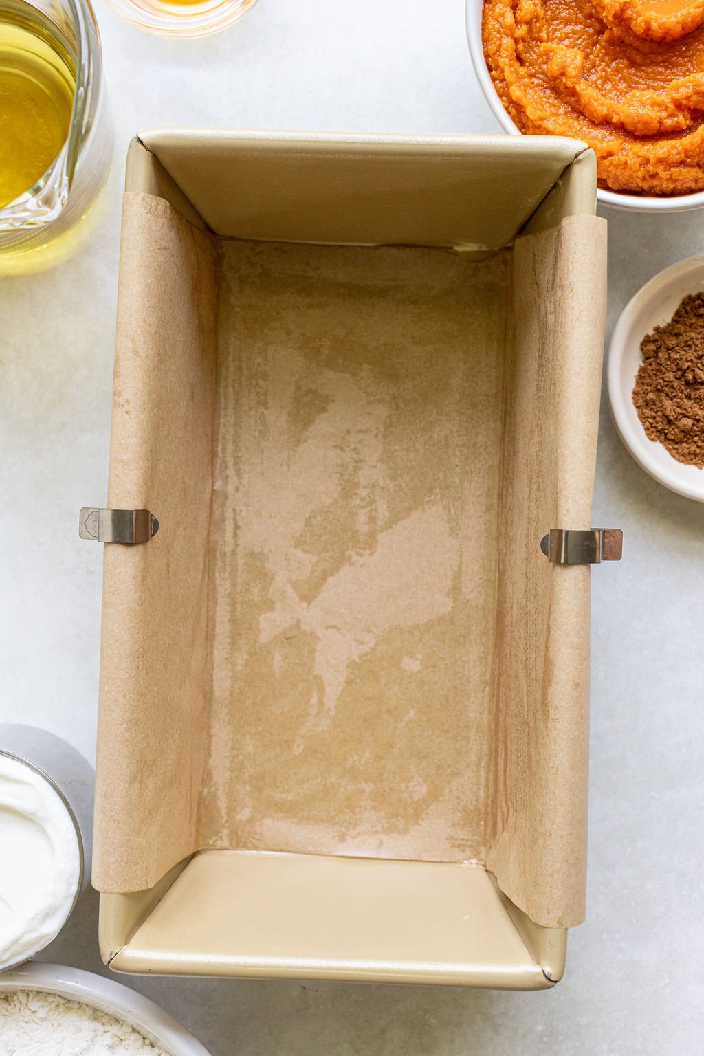 A loaf pan lined with parchment paper and metal clips on a countertop.