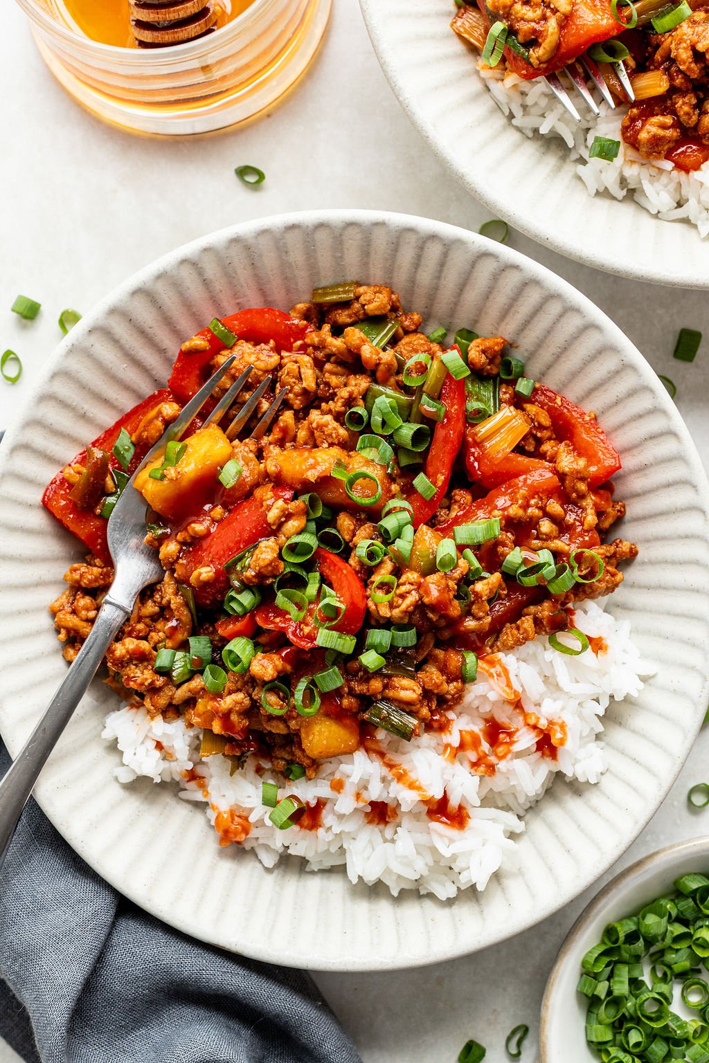 A bowl of white rice topped with ground meat, red bell peppers, green onions, and sauce, with a fork resting on the side.