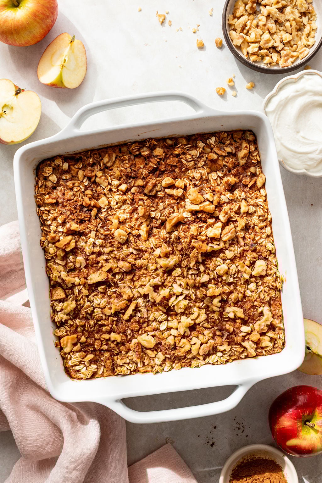 A square white baking dish filled with baked apple crisp topped with oats and nuts.