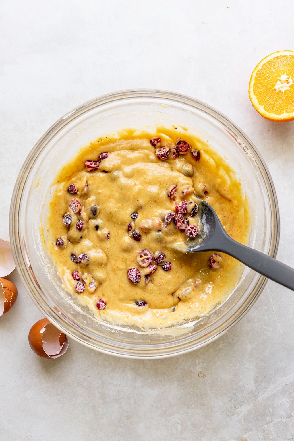A glass bowl with cranberry bread batter being mixed with a spoon.