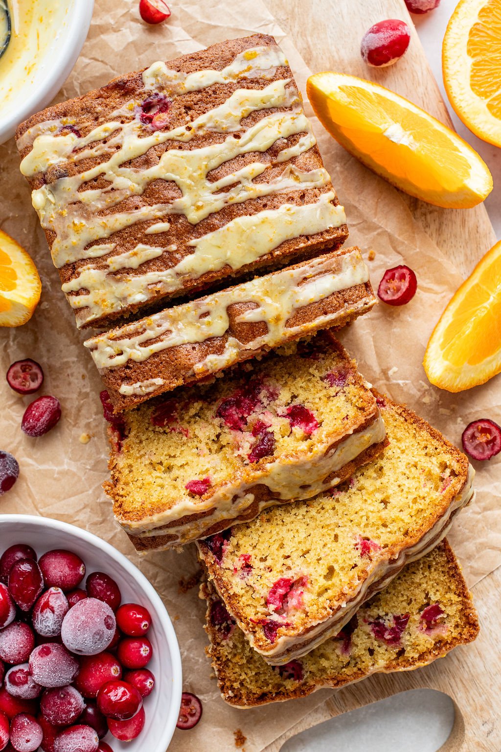 Sliced cranberry orange loaf with icing drizzle on parchment paper.