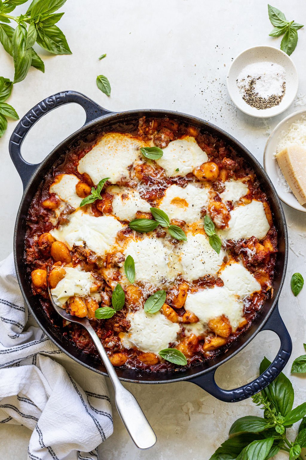 A skillet filled with baked gnocchi in tomato sauce, topped with melted cheese and fresh basil leaves, with a spoon resting in the dish.