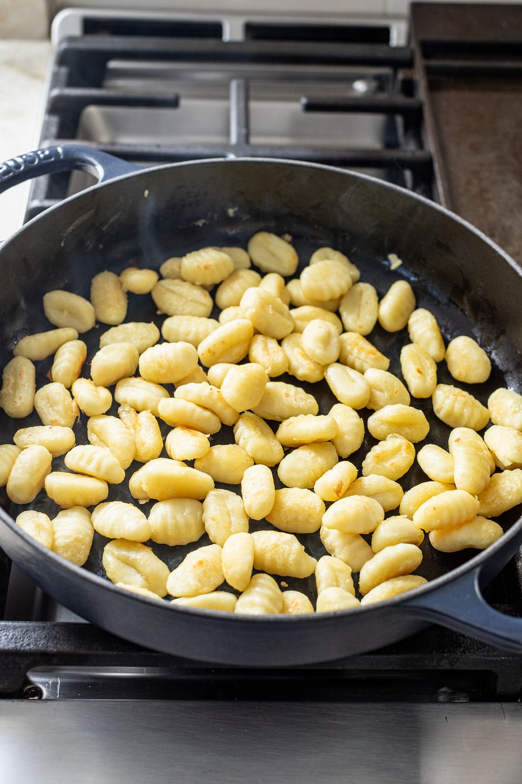 A black skillet filled with cooked gnocchi sits on a stove.