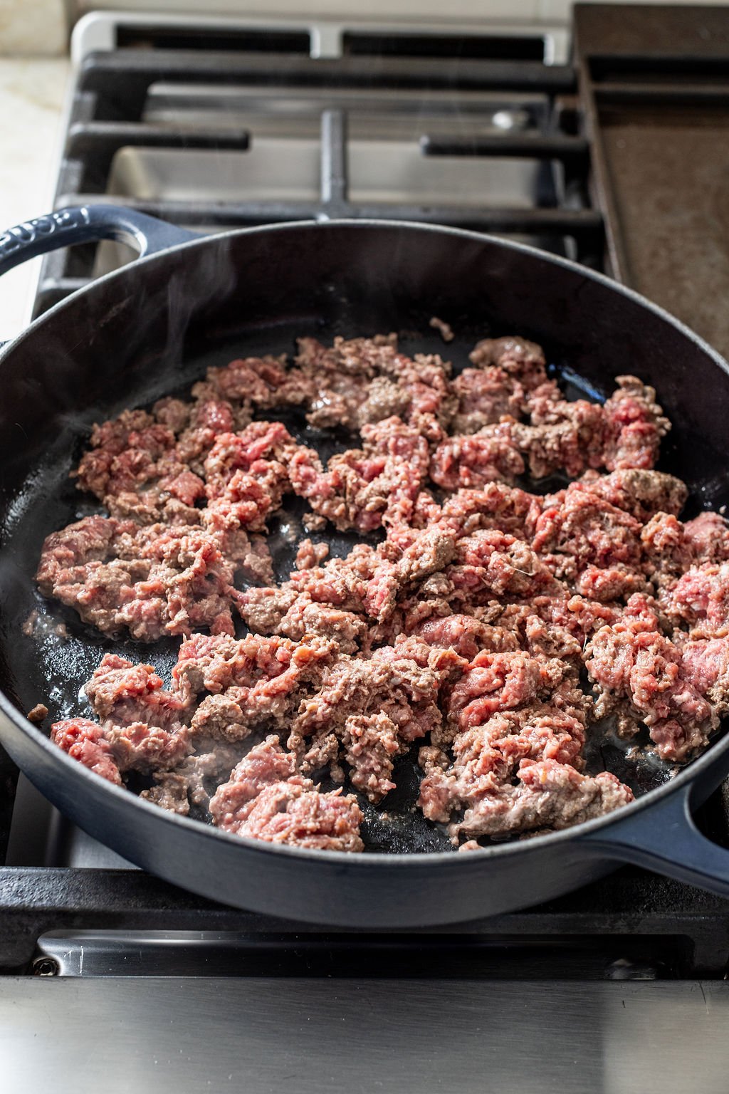 Ground beef cooking in a black skillet on a stovetop.