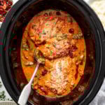 Chicken breasts in a creamy tomato sauce with spinach and herbs in a slow cooker, topped with grated cheese.