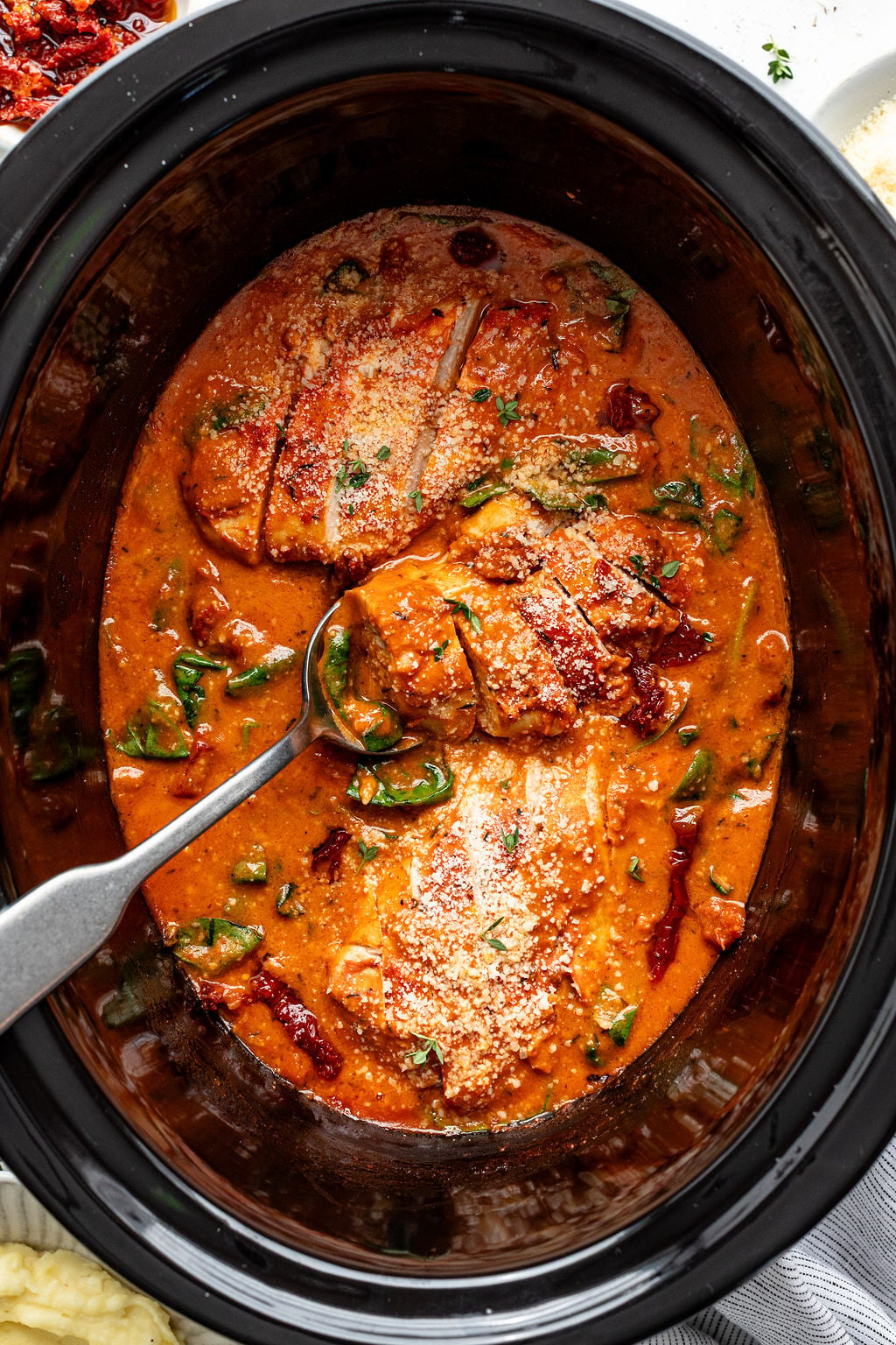 Chicken breasts in a creamy tomato sauce with spinach and herbs, served in a slow cooker with a metal serving spoon.