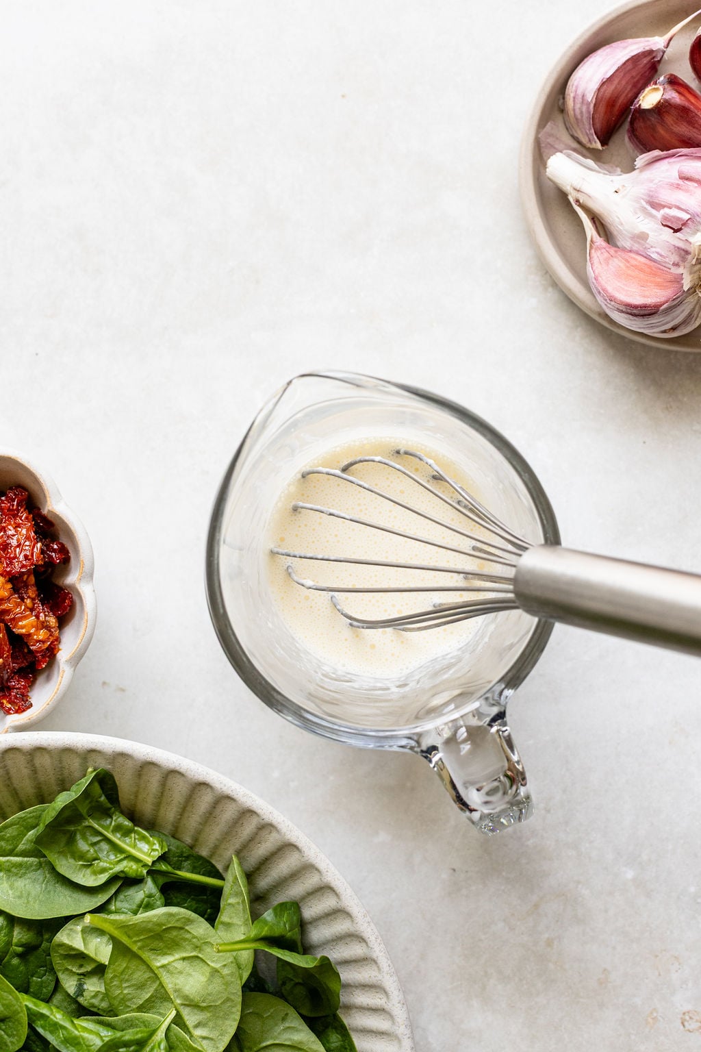A whisk in a glass measuring cup with whisked cream and cornstarch.