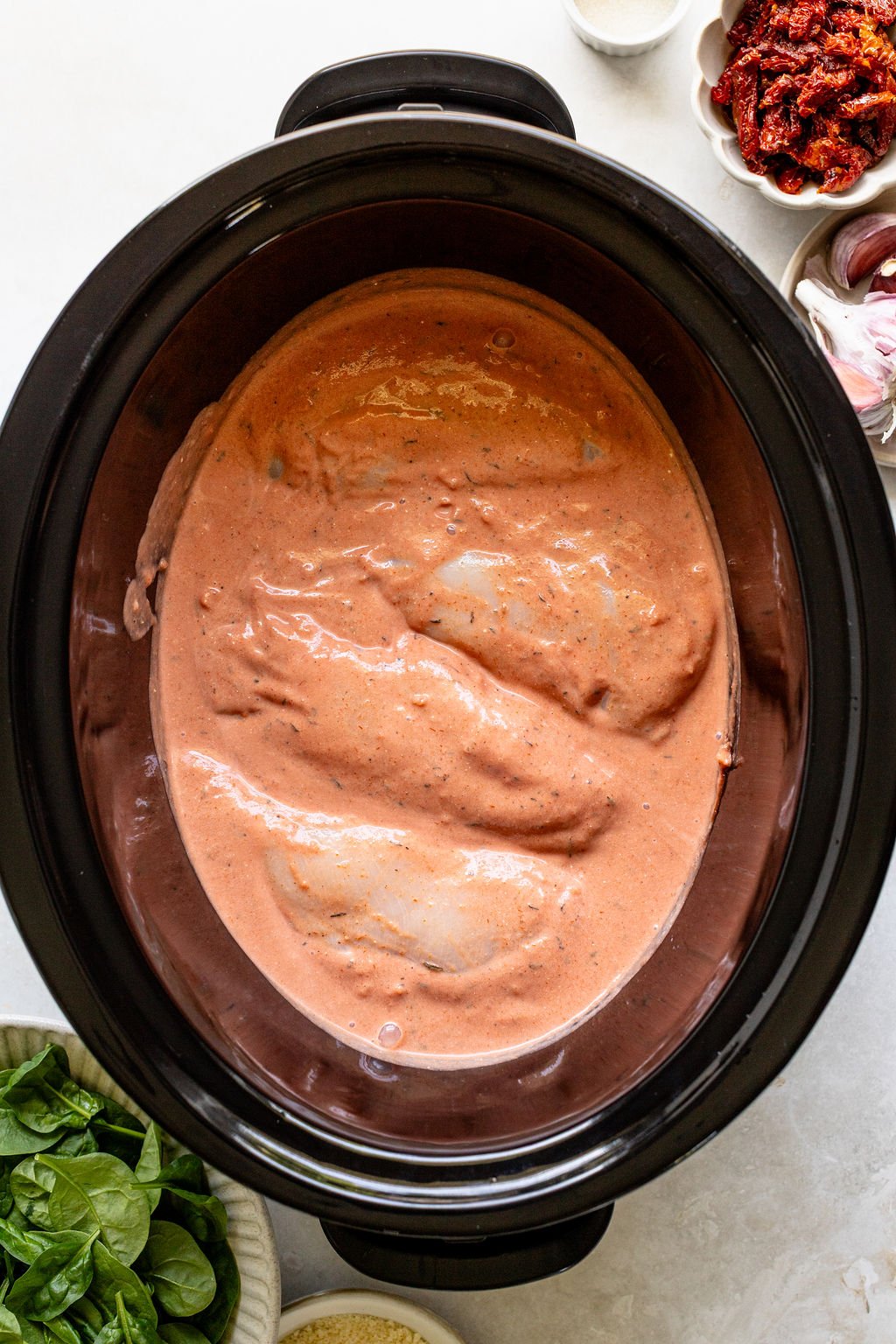Raw chicken breasts covered in a creamy tomato sauce inside a slow cooker.