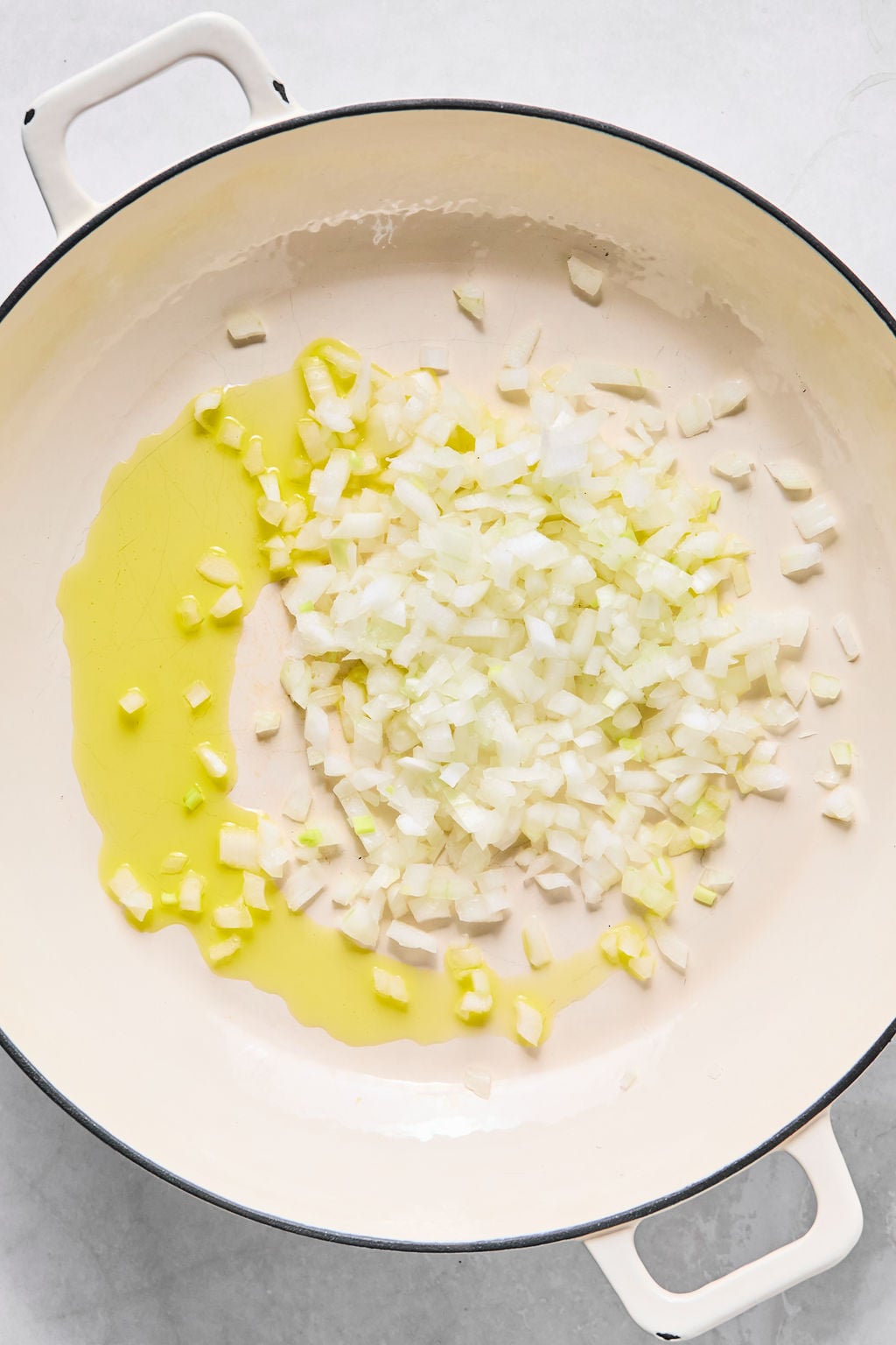 Chopped onions and olive oil in a white pot, ready to be saut&eacute;ed.