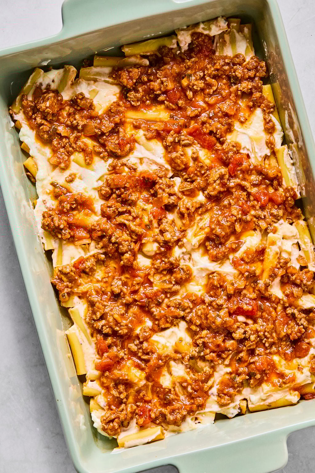 A baking dish filled with a pasta casserole layered with ricotta cheese and topped with ground meat and tomato sauce.