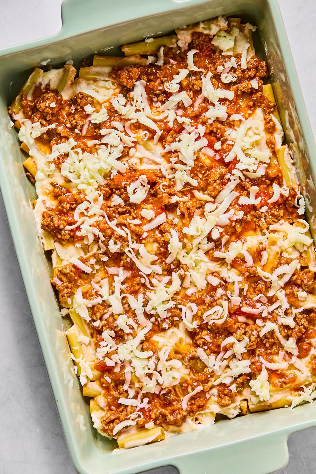 A rectangular baking dish filled with layered pasta, meat sauce, and shredded cheese.