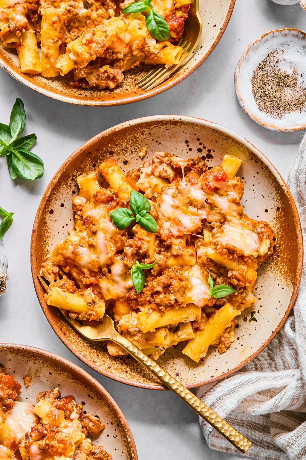 Top-down view of baked ziti with melted cheese and tomato sauce on a ceramic plate, garnished with fresh basil.