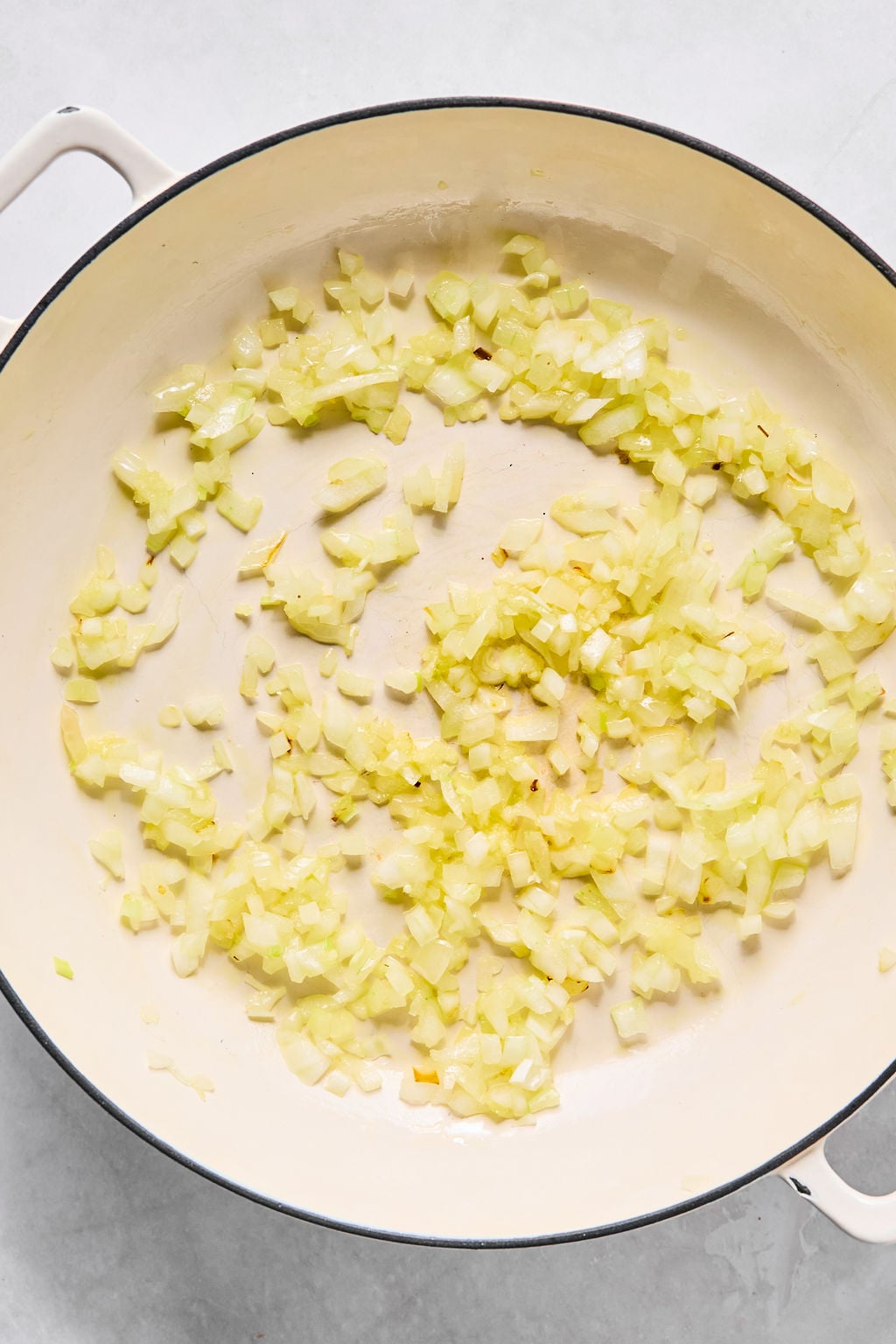 Chopped onions are saut&eacute;ing in a large, round, white skillet.