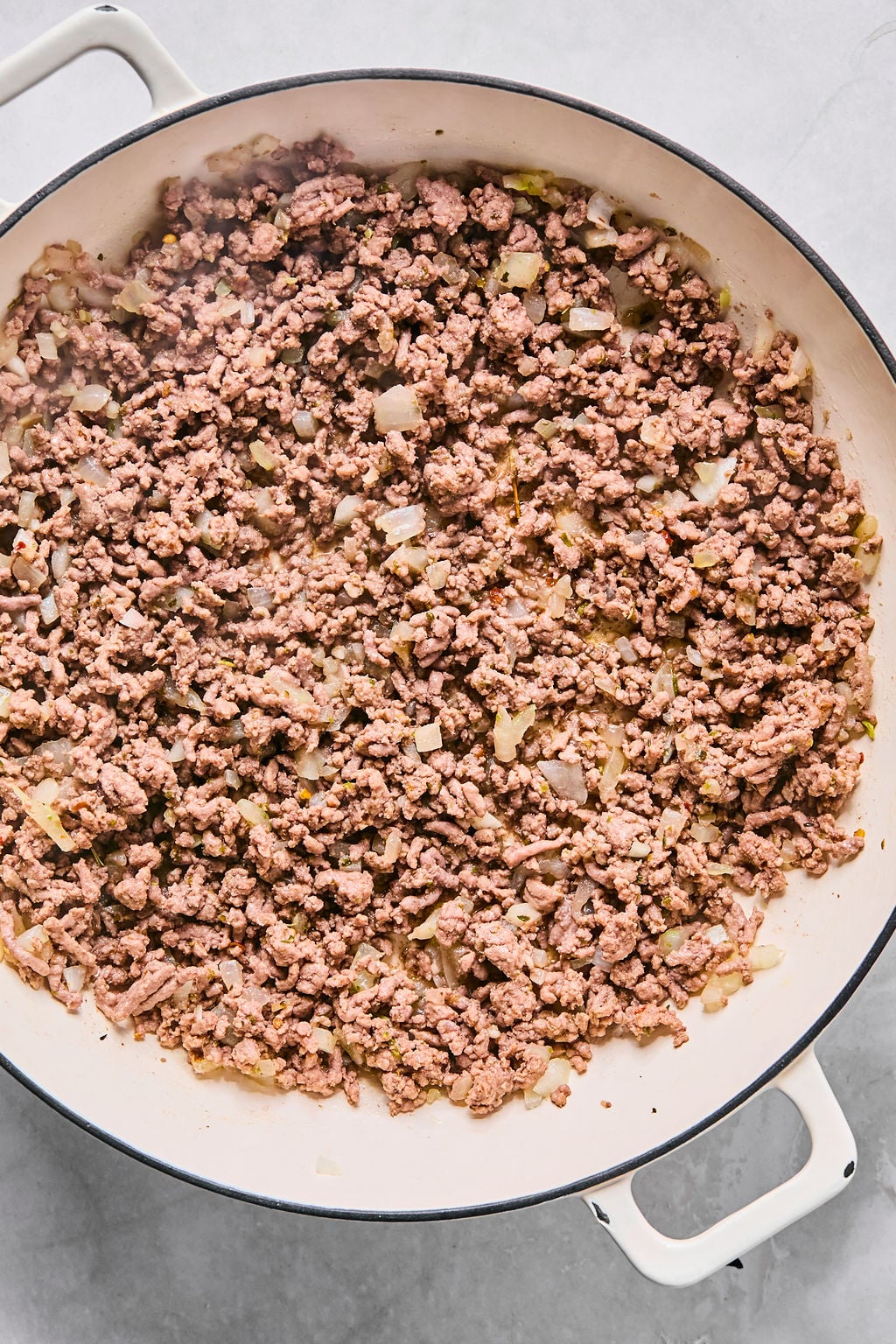 Ground beef and diced onions cooking in a large white pot on a stovetop.