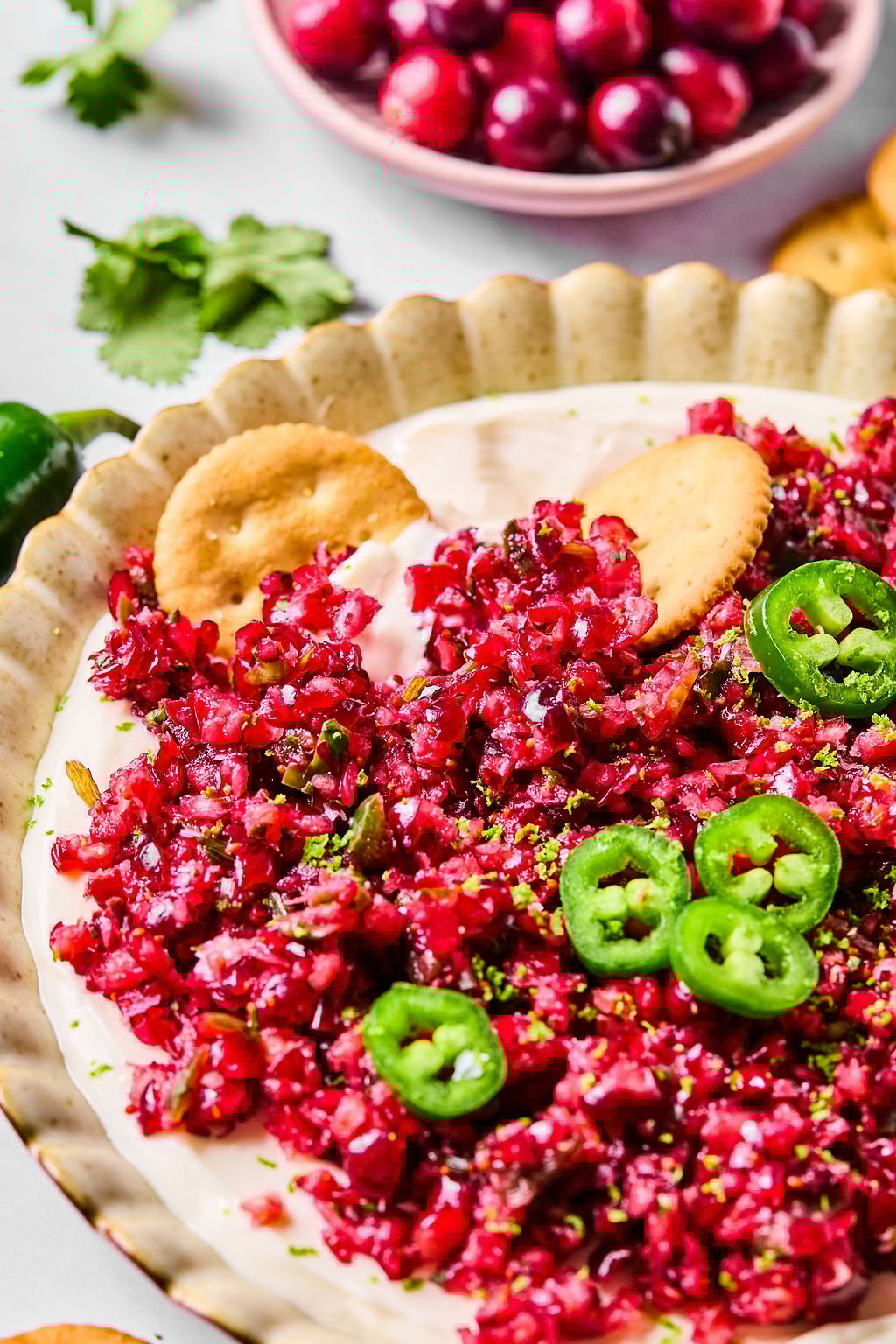 A plate of cranberry jalapeño dip topped with sliced jalapeños and served with round crackers.