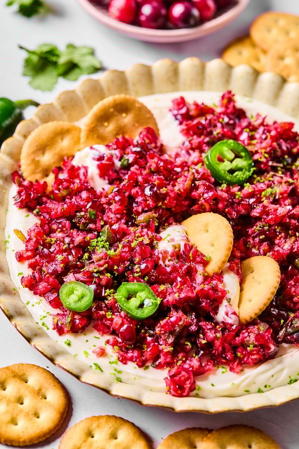 A plate of cream cheese topped with finely chopped cranberry salsa, garnished with jalapeño slices and served with round crackers.