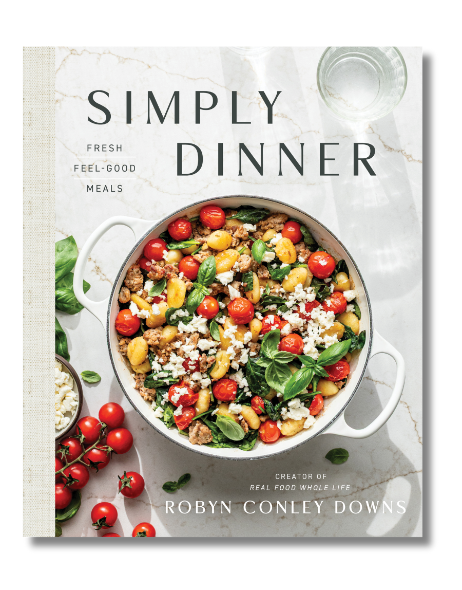 A cookbook titled Simply Dinner by Robyn Conley Downs, featuring a pot of vegetable and grain salad with tomatoes, greens, and cheese on a marble surface.