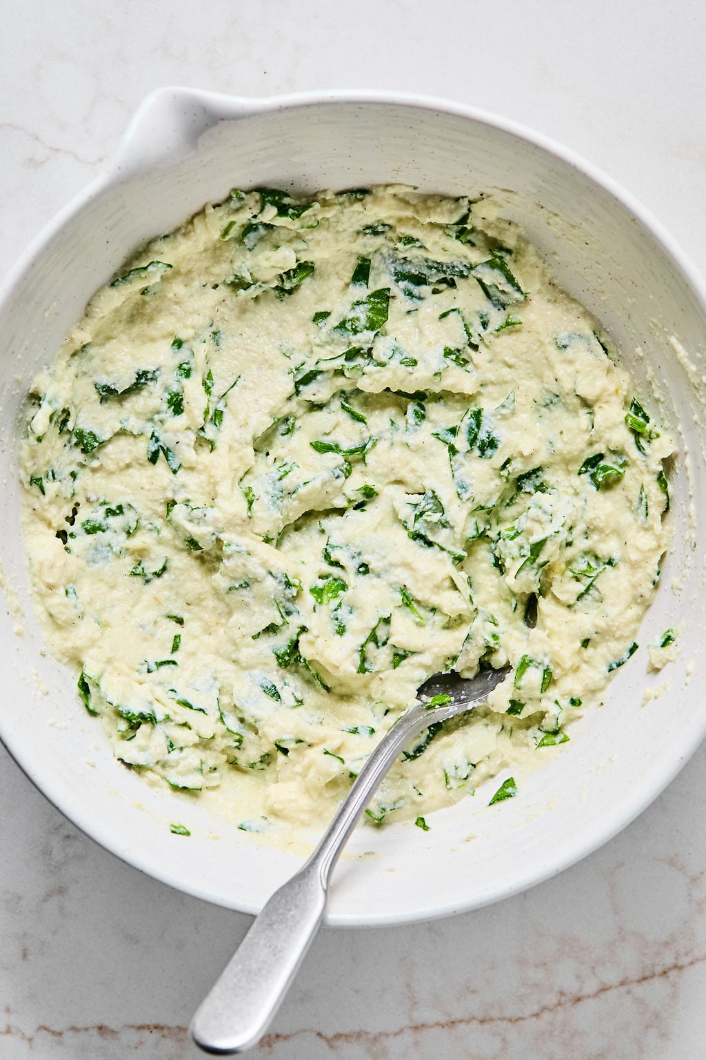 A white bowl filled with a creamy mixture containing chopped spinach.