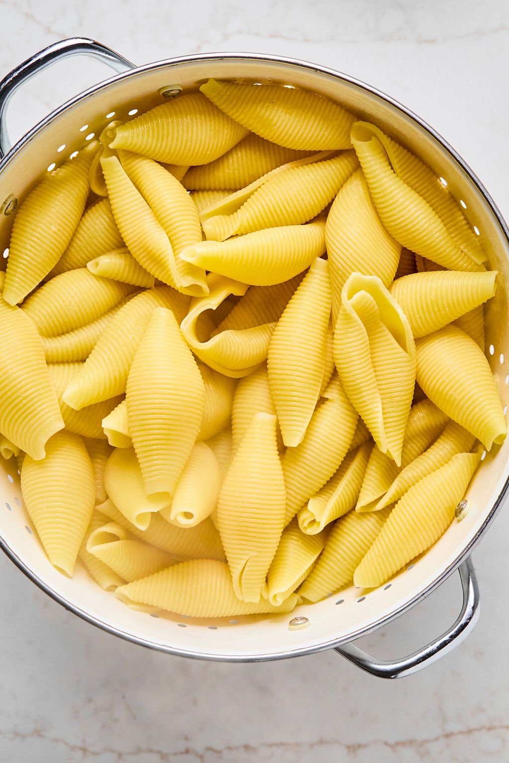Large shell pasta sits in a metal colander, freshly cooked and draining.