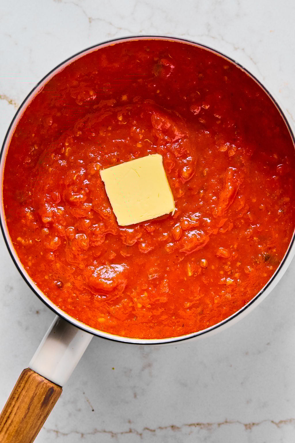 A saucepan filled with tomato sauce and a square of butter melting in the center.