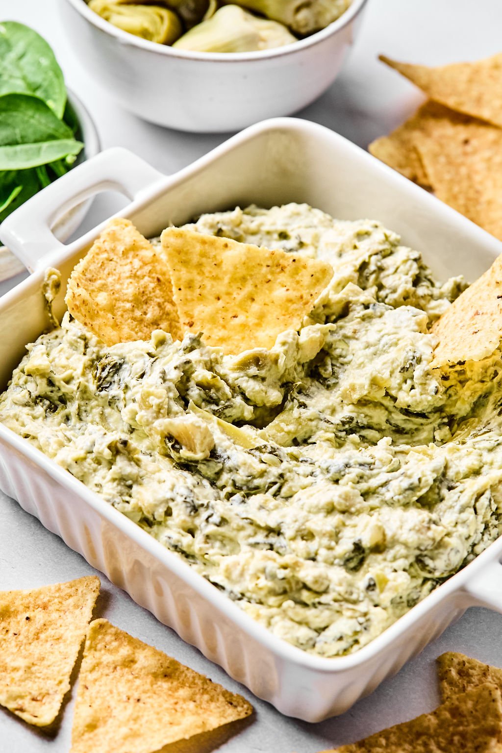 A white dish filled with spinach artichoke dip, garnished with tortilla chips.