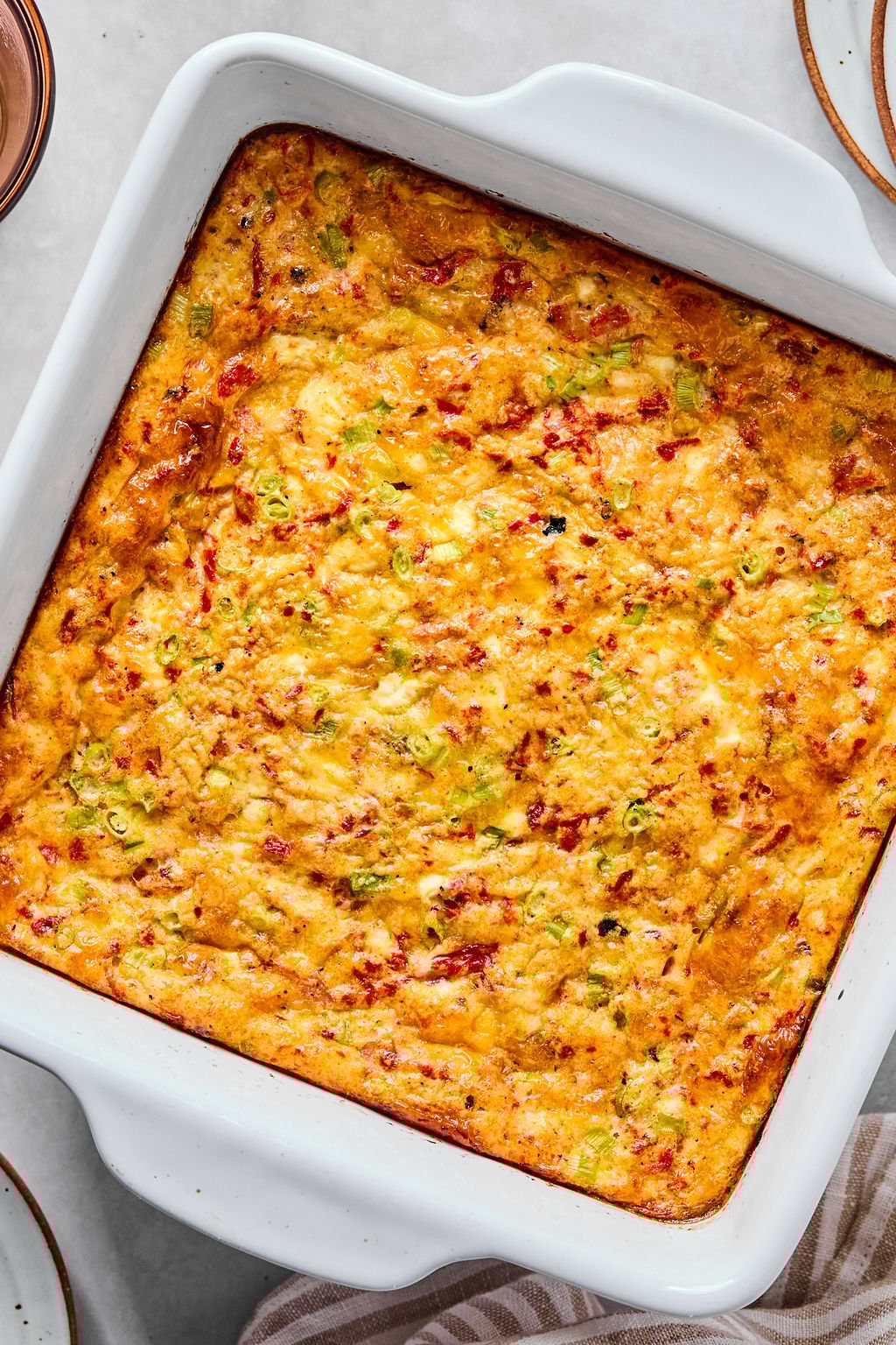 A baked egg casserole dish filled with a golden-brown, cheesy mixture, featuring visible bits of green onions and red peppers.