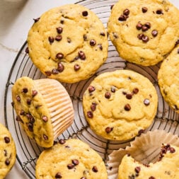 A cooling rack with several chocolate chip muffins, one with a bite taken out.