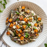 A bowl of salad with roasted sweet potato, shredded chicken, red onions, crumbled cheese, and chopped parsley, with a fork on the side.