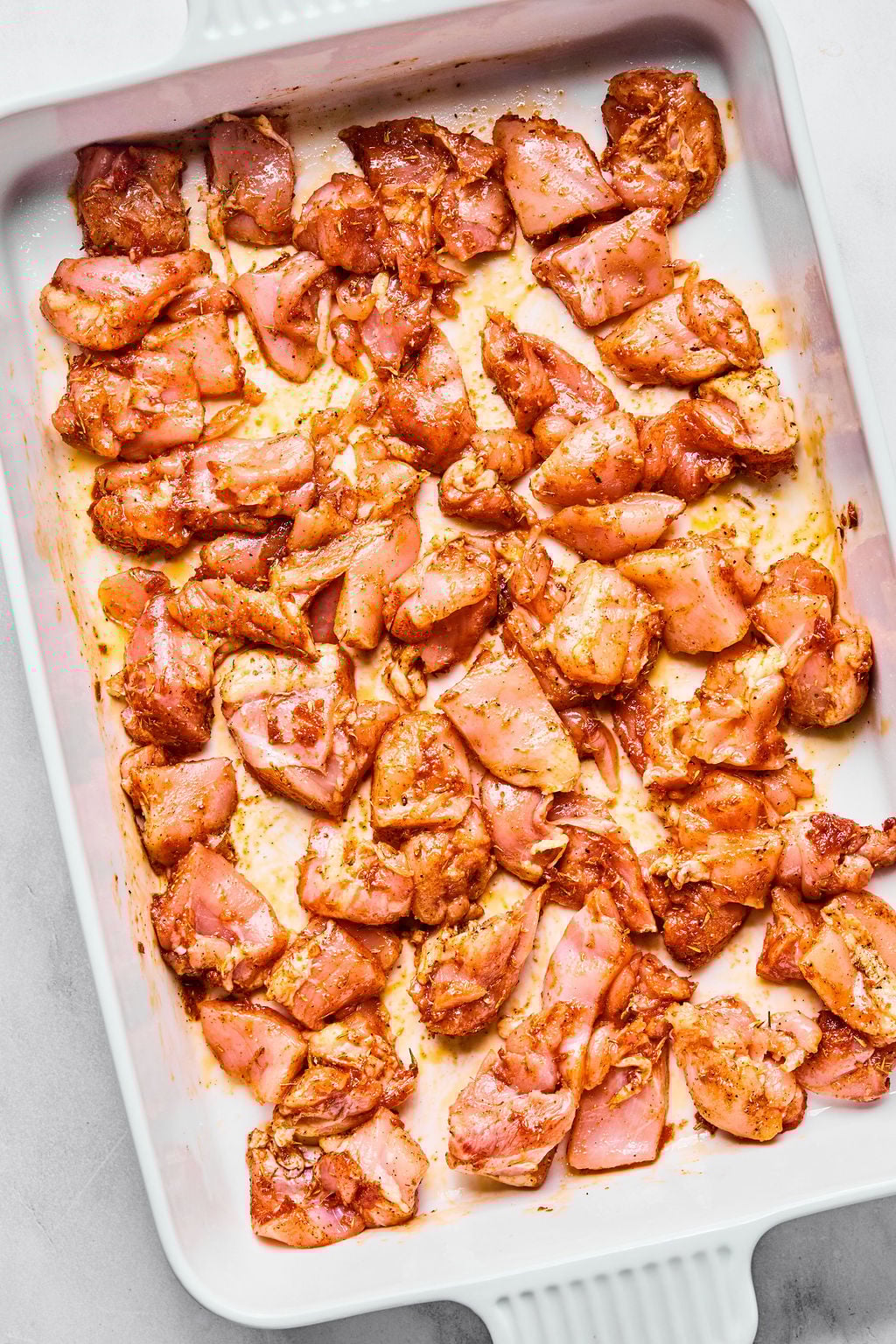 Raw, marinated pieces of chicken arranged in a single layer inside a white rectangular baking dish.